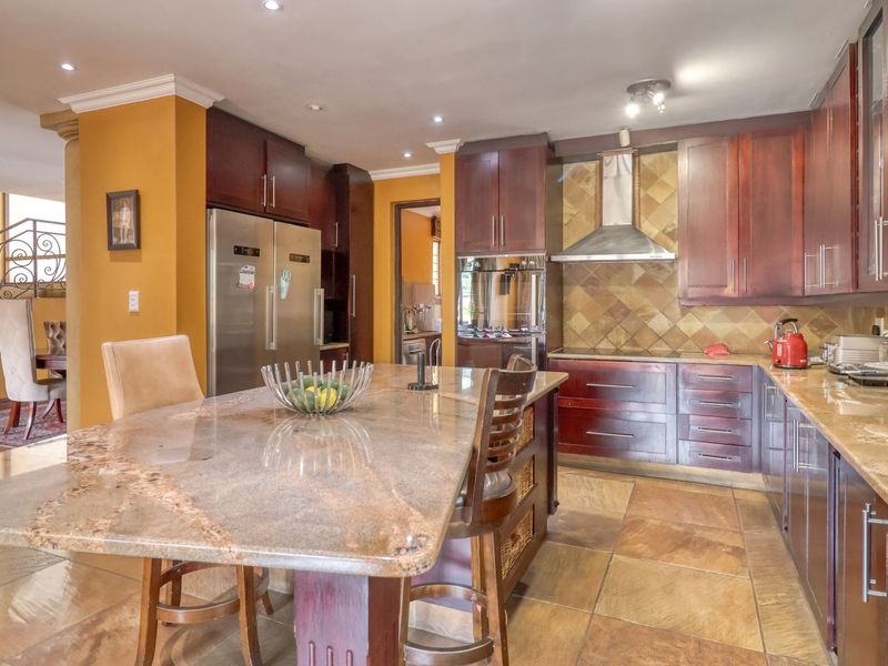 Spacious kitchen featuring dark wood cabinetry, granite countertops, a central island, and tiled flooring, with an open-plan layout leading to the staircase area.