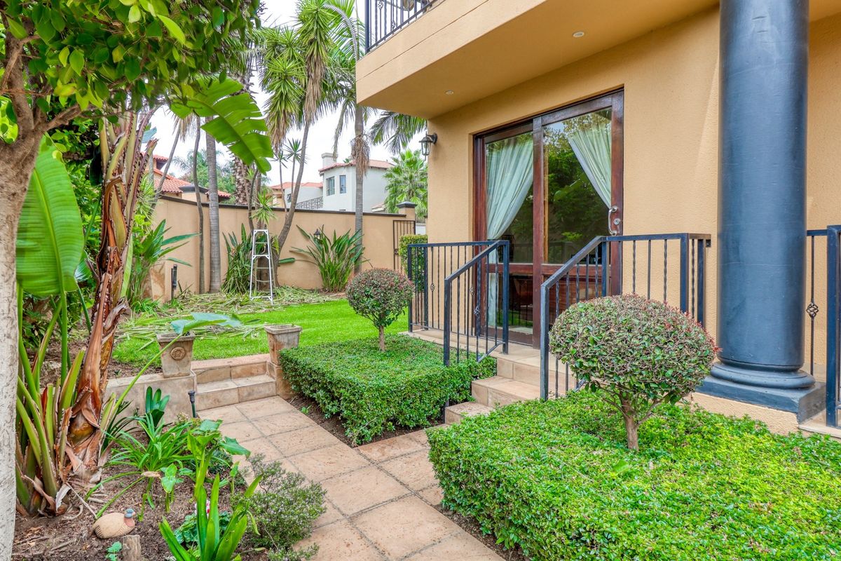 A well-maintained rear garden area featuring a paved walkway, manicured hedges, and direct access to the home via sliding glass doors.