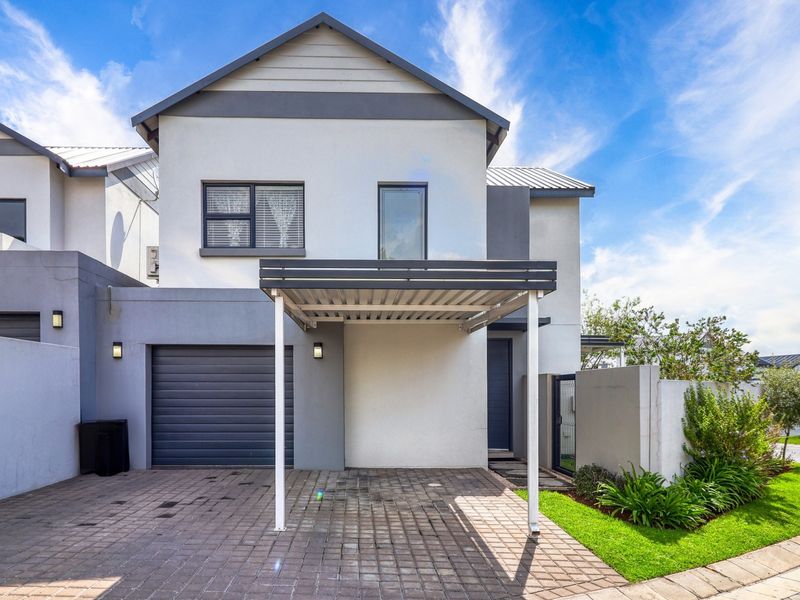 Front elevation of a modern cluster home featuring a paved driveway, covered carport, single garage, and a neat landscaped garden area.