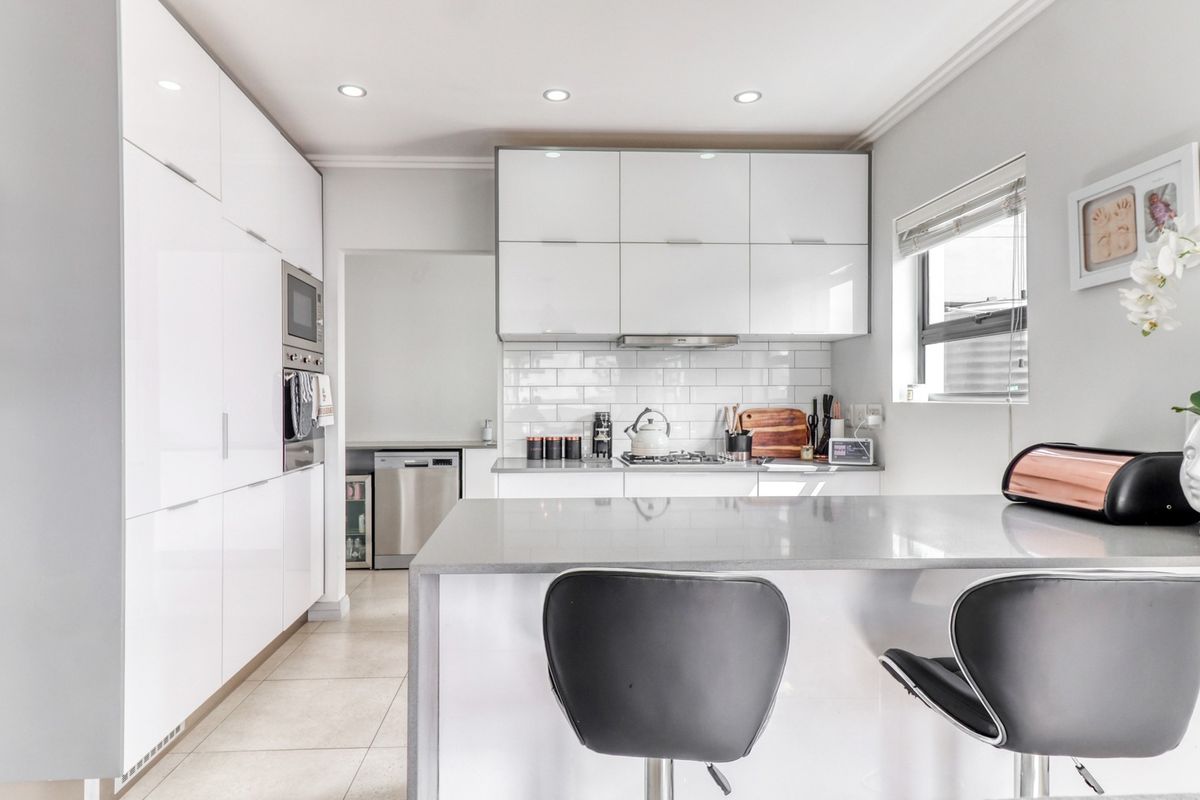 Modern kitchen featuring high-gloss white cabinetry, stone countertops, subway tile backsplash, and integrated appliances with a breakfast bar island.