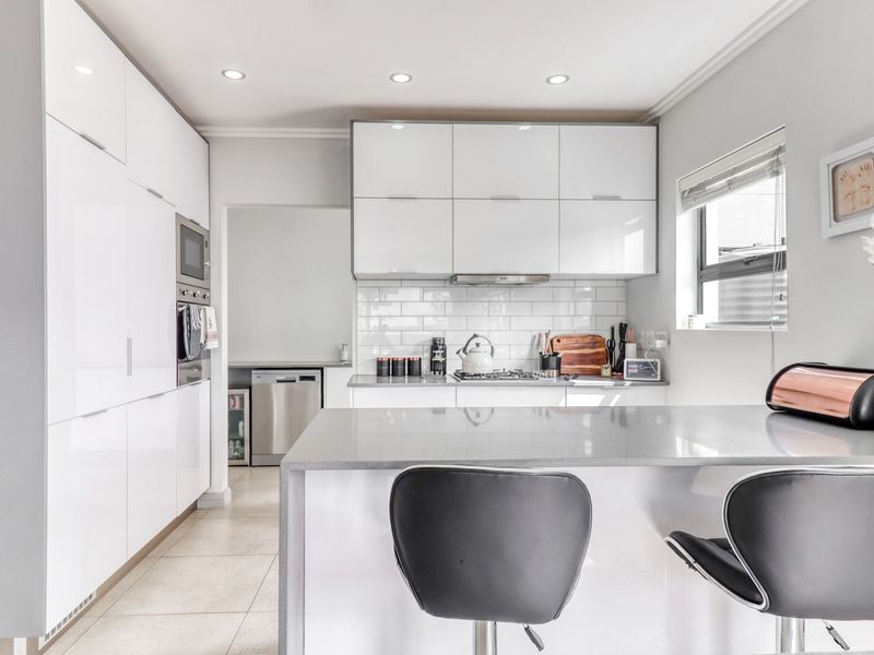 Modern kitchen featuring high-gloss white cabinetry, stone countertops, subway tile backsplash, and integrated appliances with a breakfast bar island.
