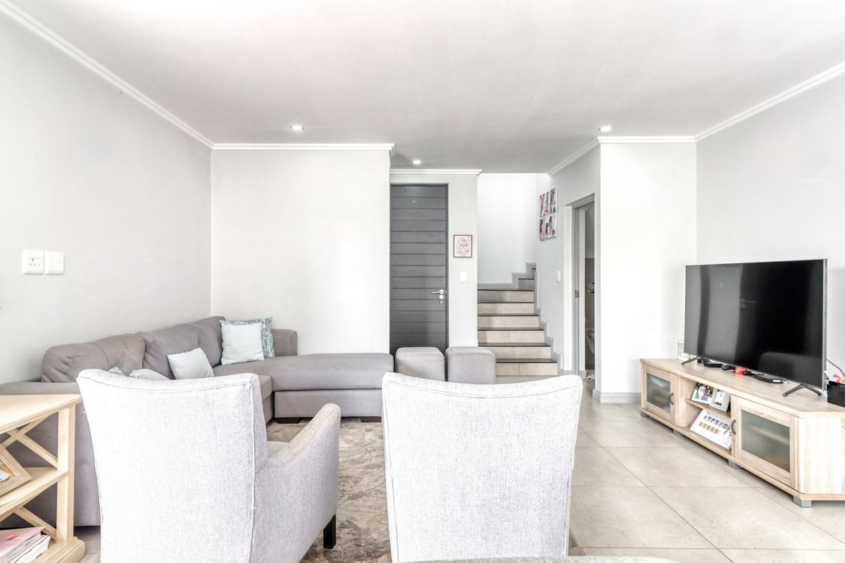 A bright and spacious living room featuring neutral tiled flooring, recessed downlighting, and a staircase leading to the upper level.