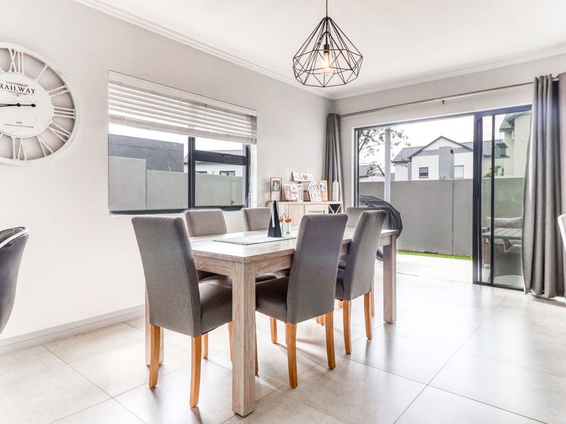 Bright dining area featuring large format floor tiles, modern pendant lighting, and sliding glass doors providing seamless access to the outdoor patio area.