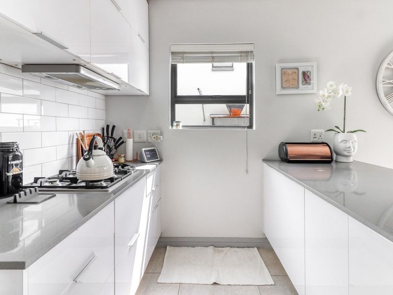 Modern galley-style kitchen featuring sleek white cabinetry, stone countertops, a gas hob with extractor fan, and a classic subway tile backsplash.