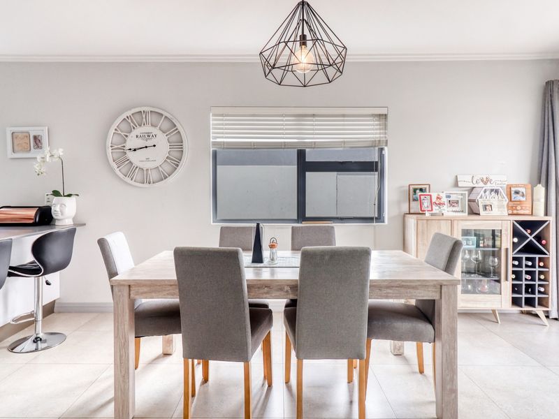 A bright open-plan dining and kitchen area featuring modern tile flooring, aluminium window frames, and a stylish geometric pendant light fixture.