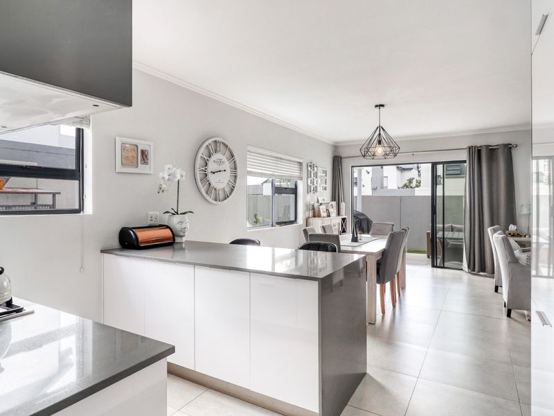 Modern open-plan living area featuring a sleek kitchen with stone countertops, gas hob, and seamless flow to the outdoor patio through sliding glass doors.