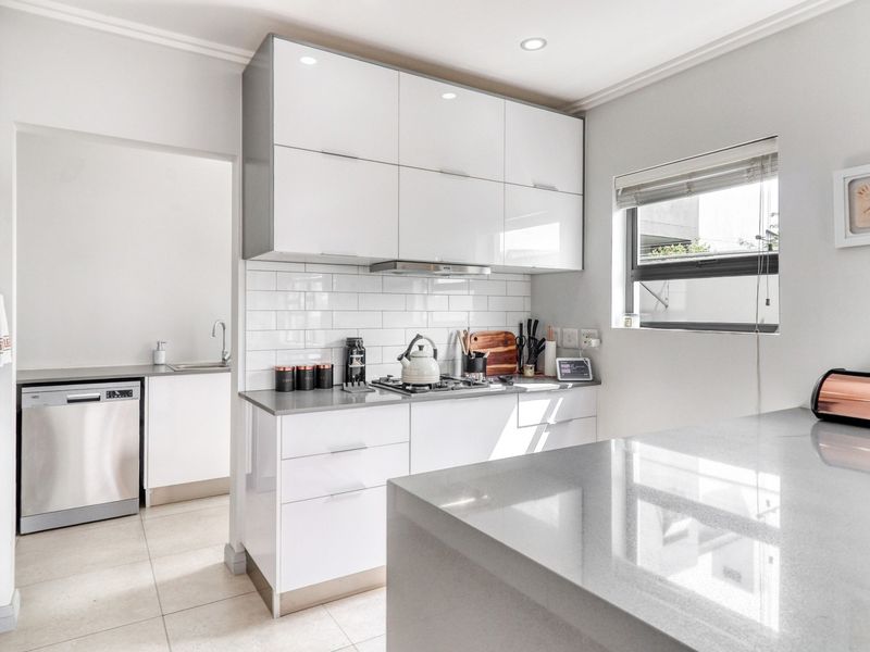 Modern kitchen featuring high-gloss cabinetry, quartz countertops, subway tile backsplash, and integrated appliances, with an adjacent scullery area.