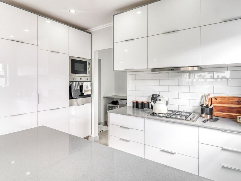 Modern kitchen featuring high-gloss white cabinetry, quartz countertops, subway tile backsplash, and integrated stainless steel appliances including a gas hob and oven.