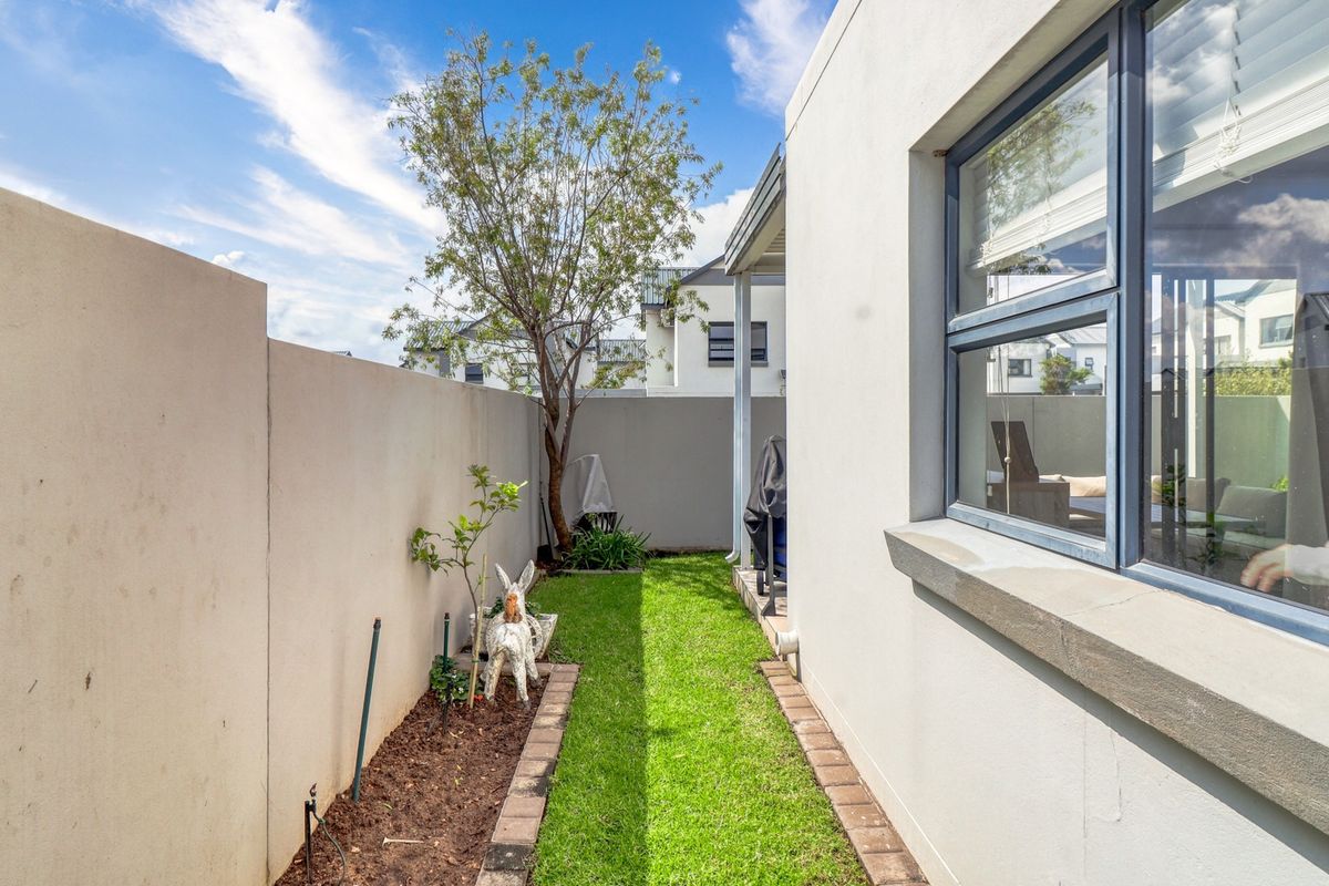 A neat and well-maintained rear garden area featuring a manicured lawn, paved edging, and high boundary walls for privacy.