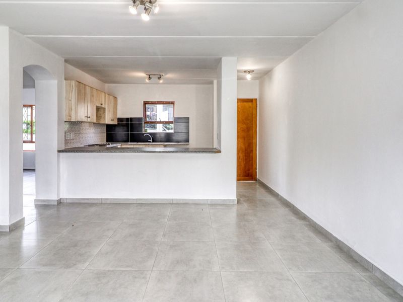 An open-plan living and kitchen area featuring neutral tiled flooring, built-in cabinetry, and a breakfast counter, offering a clean and versatile living space.