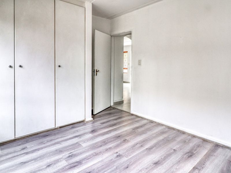 An empty bedroom featuring light-toned laminate flooring and built-in cupboards, offering a clean, neutral canvas for personalization.