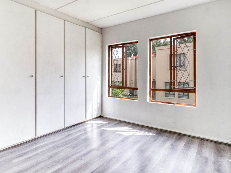 An empty bedroom featuring laminate flooring, built-in cupboards, and wooden-framed windows with security bars, offering a clean and neutral space.