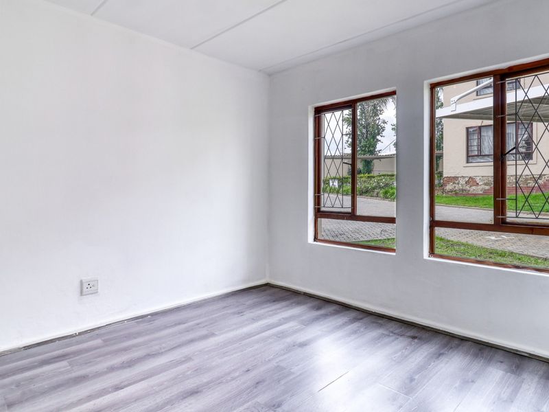 A bright, empty bedroom featuring modern grey laminate flooring, white walls, and timber-framed windows with security bars overlooking the exterior.
