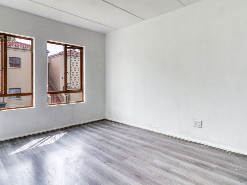 A bright, empty bedroom featuring modern grey laminate flooring, timber-framed windows with security bars, and neutral white walls.