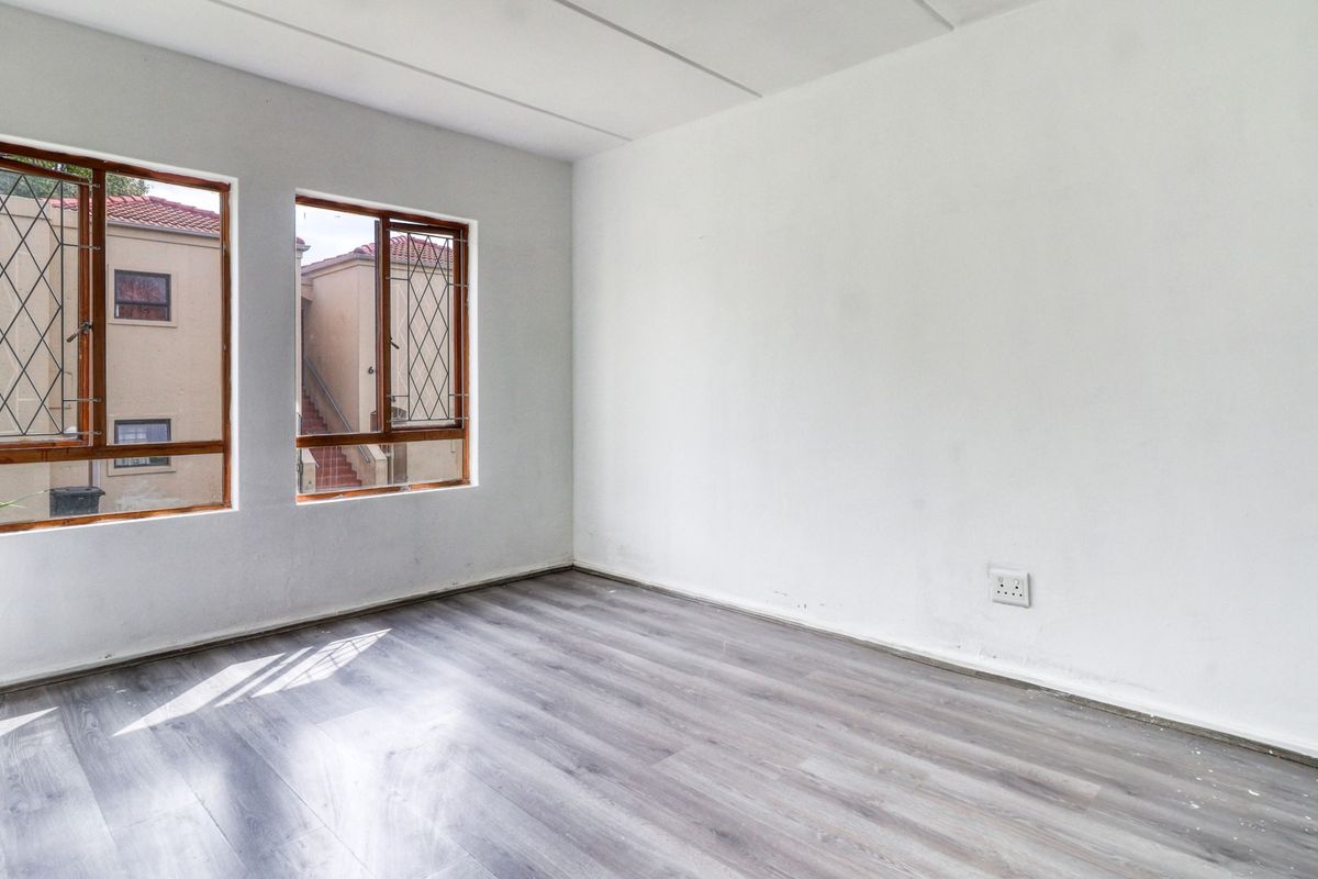 A bright, empty bedroom featuring modern grey laminate flooring, timber-framed windows with security bars, and neutral white walls.