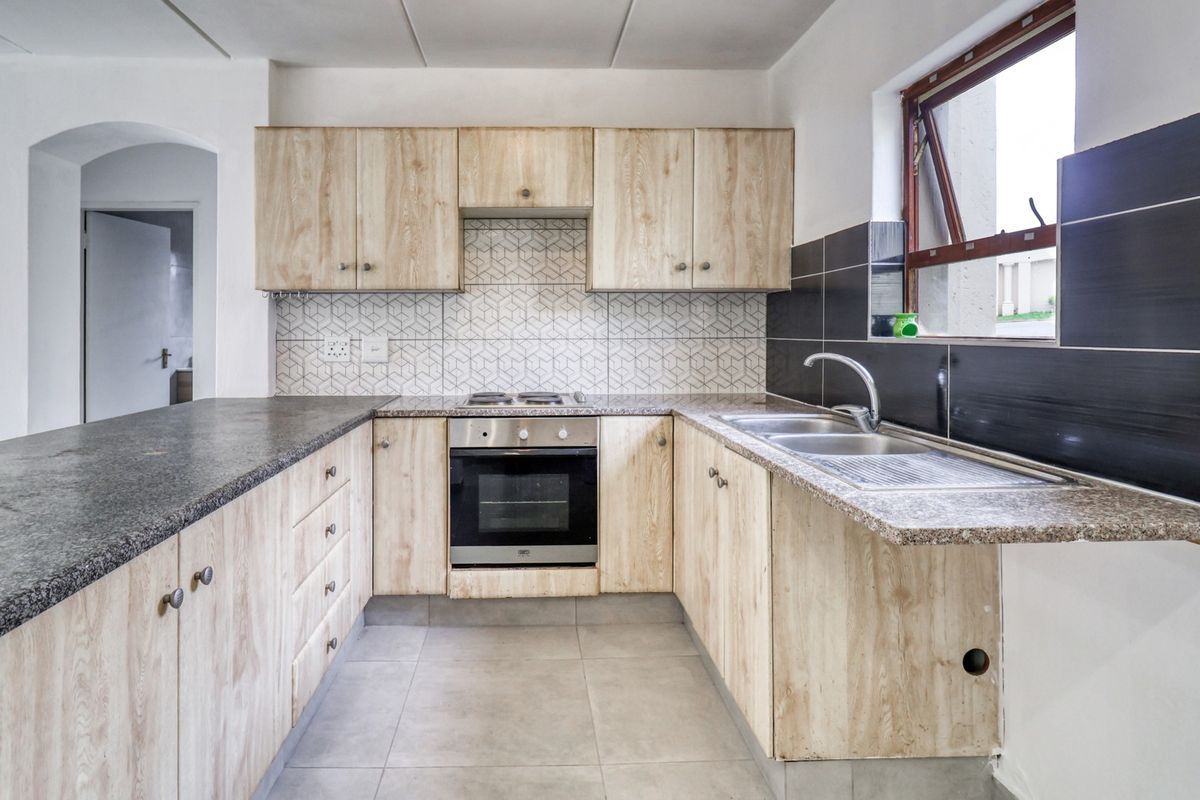 A functional kitchen featuring light wood-finish cabinetry, granite countertops, a built-in oven and hob, and a tiled backsplash.