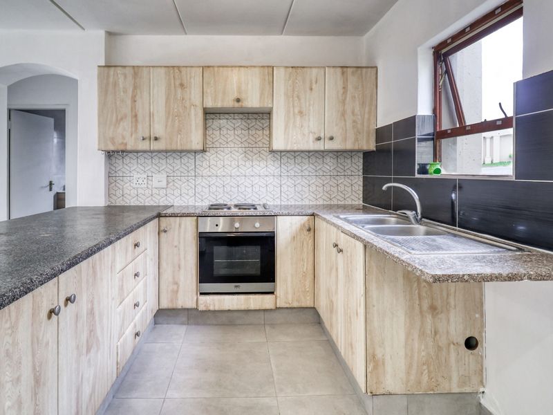 A functional kitchen featuring light wood-finish cabinetry, granite countertops, a built-in oven and hob, and a tiled backsplash.