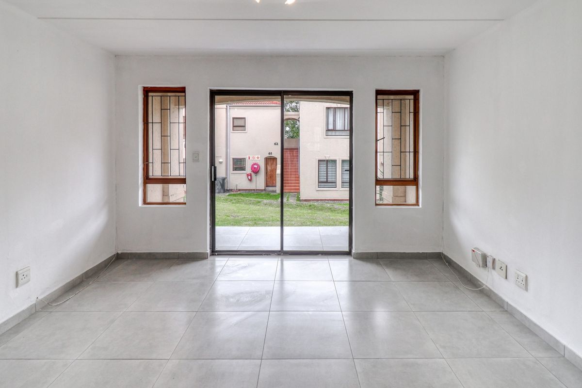An empty, well-lit living room featuring neutral tiled flooring and a sliding glass door providing access to the exterior.