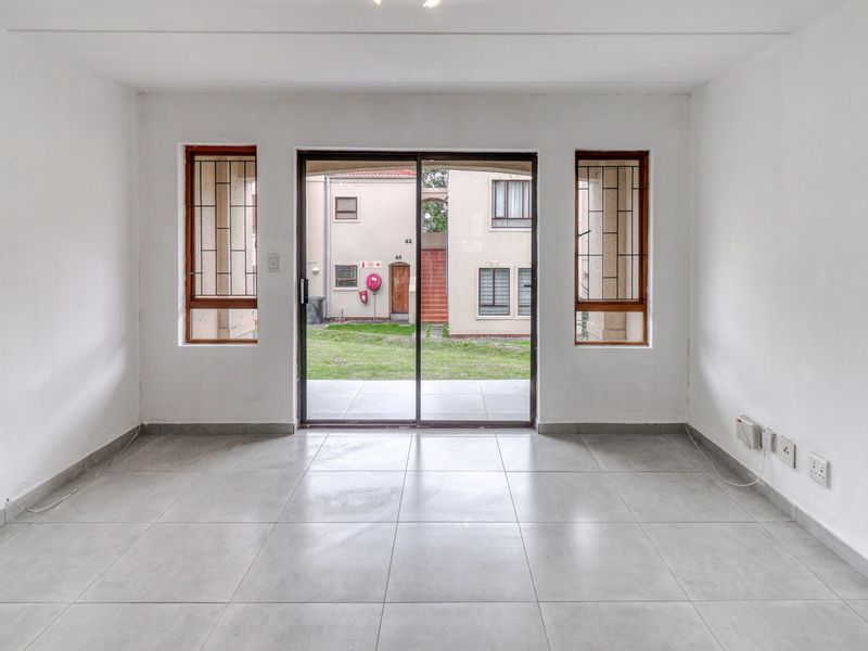 An empty, well-lit living room featuring neutral tiled flooring and a sliding glass door providing access to the exterior.