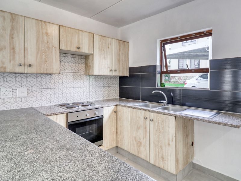 A clean, modern kitchen featuring light wood-finish cabinetry, granite countertops, a built-in oven and hob, and a stainless steel double sink.