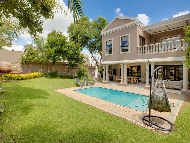 A well-maintained rear garden featuring a swimming pool, stone water feature, covered patio area, and a two-story residence with a balcony.