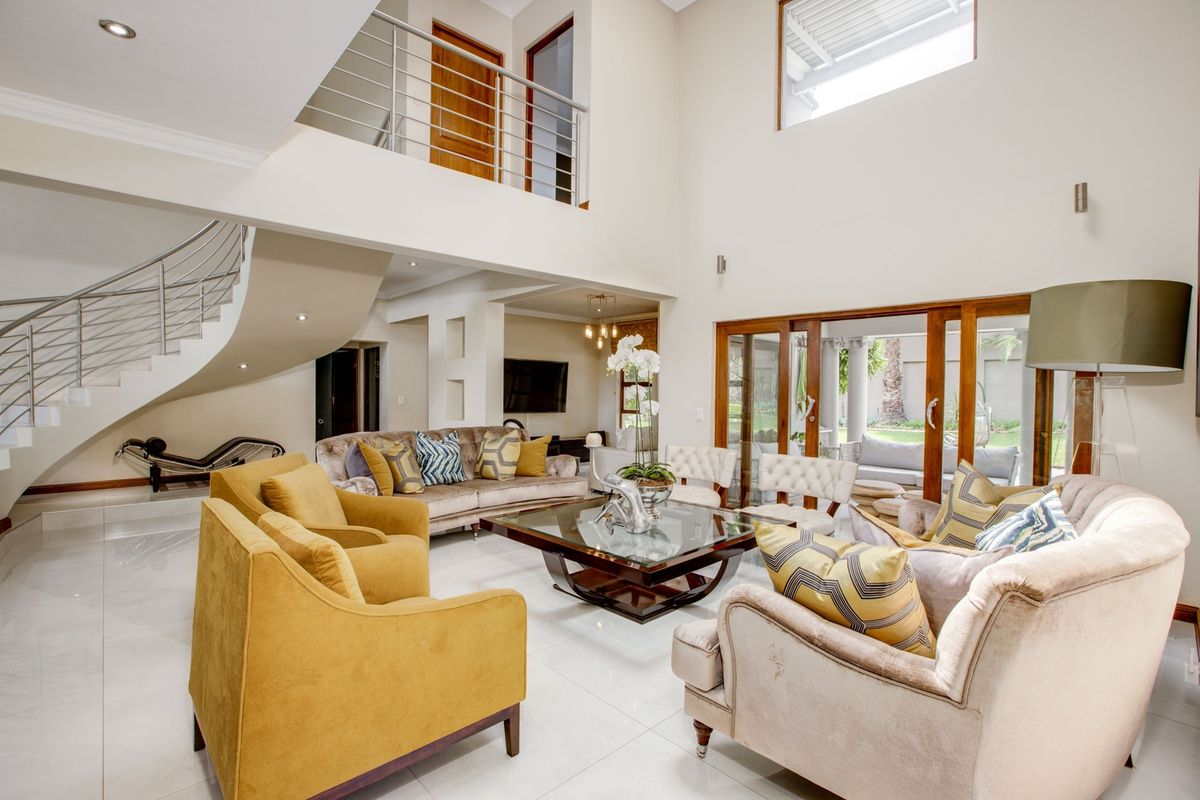 Spacious double-volume living room featuring a striking curved staircase, polished tile flooring, and large sliding doors providing seamless access to the outdoor patio area.