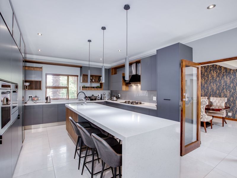 Modern kitchen featuring a large quartz island, sleek grey cabinetry, built-in appliances, and high-quality porcelain floor tiles with recessed lighting.