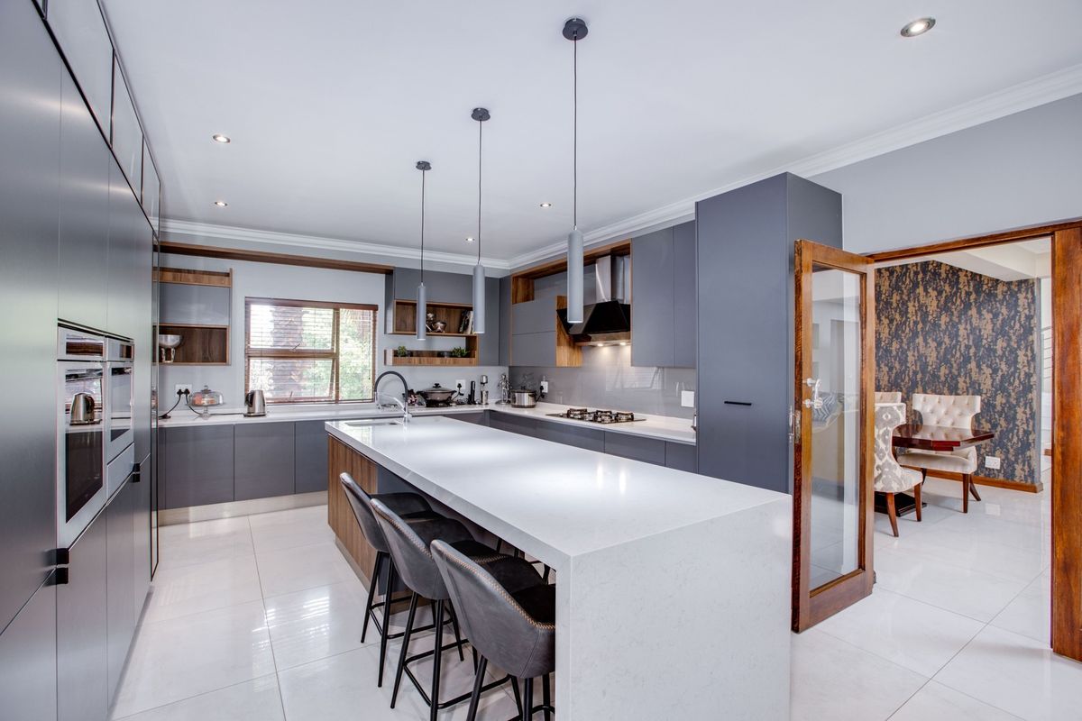 Modern kitchen featuring a large quartz island, sleek grey cabinetry, built-in appliances, and high-quality porcelain floor tiles with recessed lighting.
