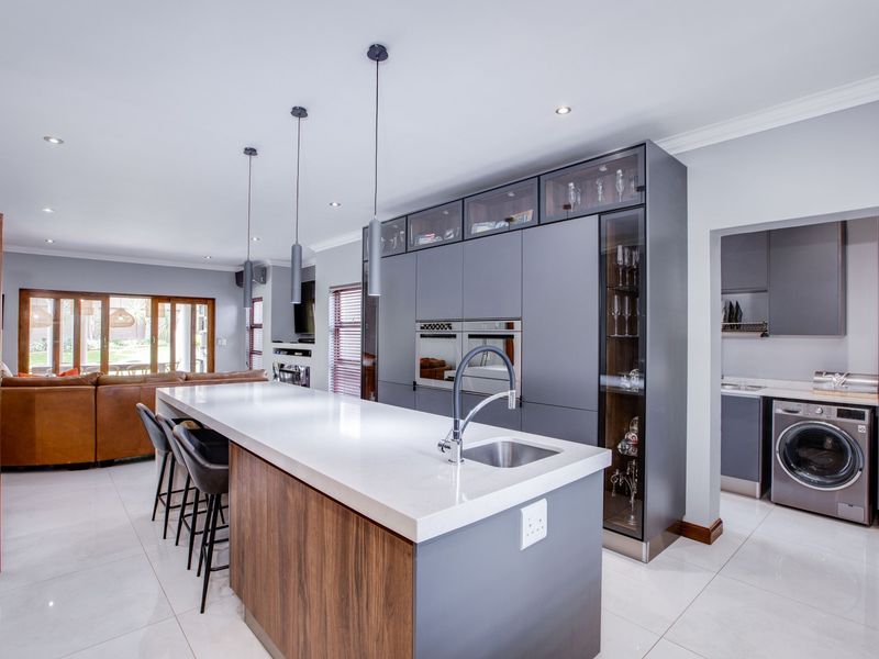 Modern open-plan kitchen featuring a large island with stone countertops, integrated appliances, and an adjacent scullery with laundry facilities.