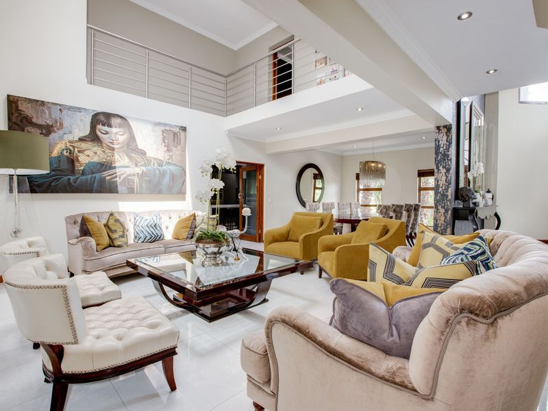Spacious open-plan living and dining area featuring a double-volume ceiling, mezzanine level with metal balustrade, and polished tiled flooring.