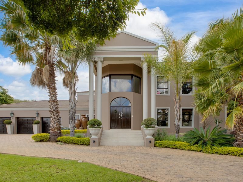 Impressive double-story residence featuring a grand portico entrance, arched double doors, and a paved driveway leading to a double garage.