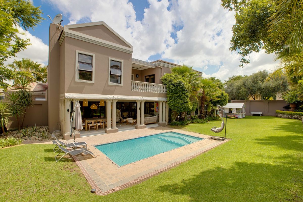 Rear view of a two-story house featuring a swimming pool, covered patio, and balcony overlooking a well-maintained garden.