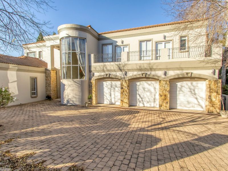 A well-maintained double-story residence featuring a triple garage, stone-clad accents, a paved driveway, and an upper-level balcony with wrought iron railings.