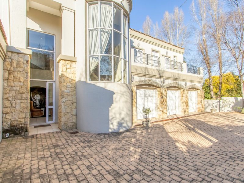 A grand front facade featuring stone cladding, a triple garage, and a striking curved bay window with a balcony above.