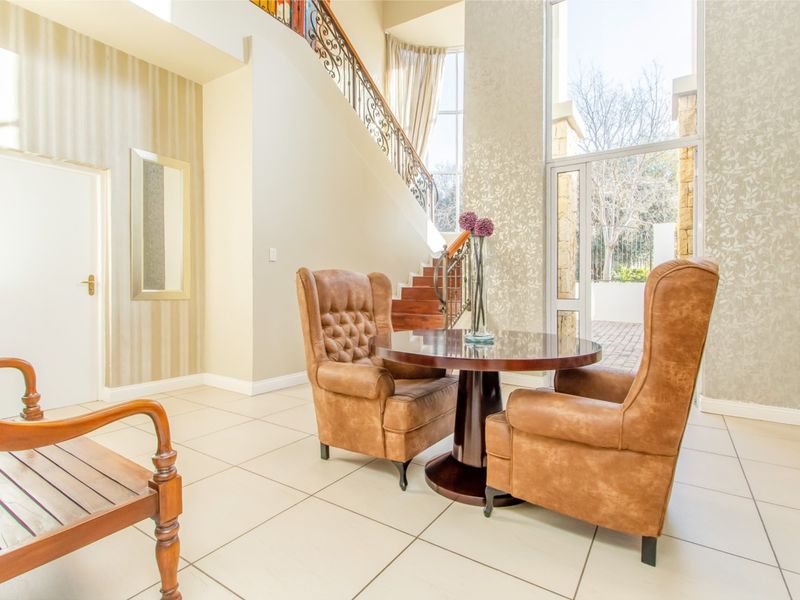 Spacious double-volume entrance hall featuring elegant tiled flooring, a decorative wrought iron staircase, and large windows providing abundant natural light.