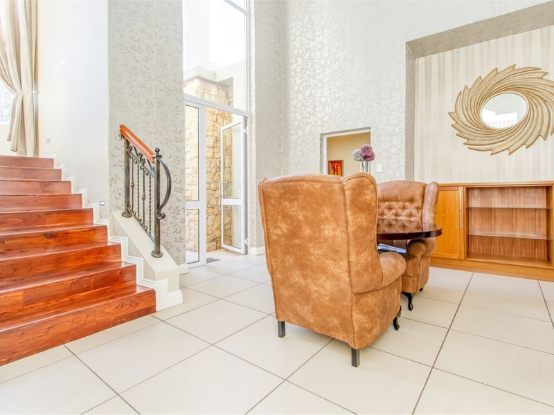 Spacious double-volume entrance hall featuring a wooden staircase with wrought iron balustrade, tiled flooring, and built-in cabinetry.