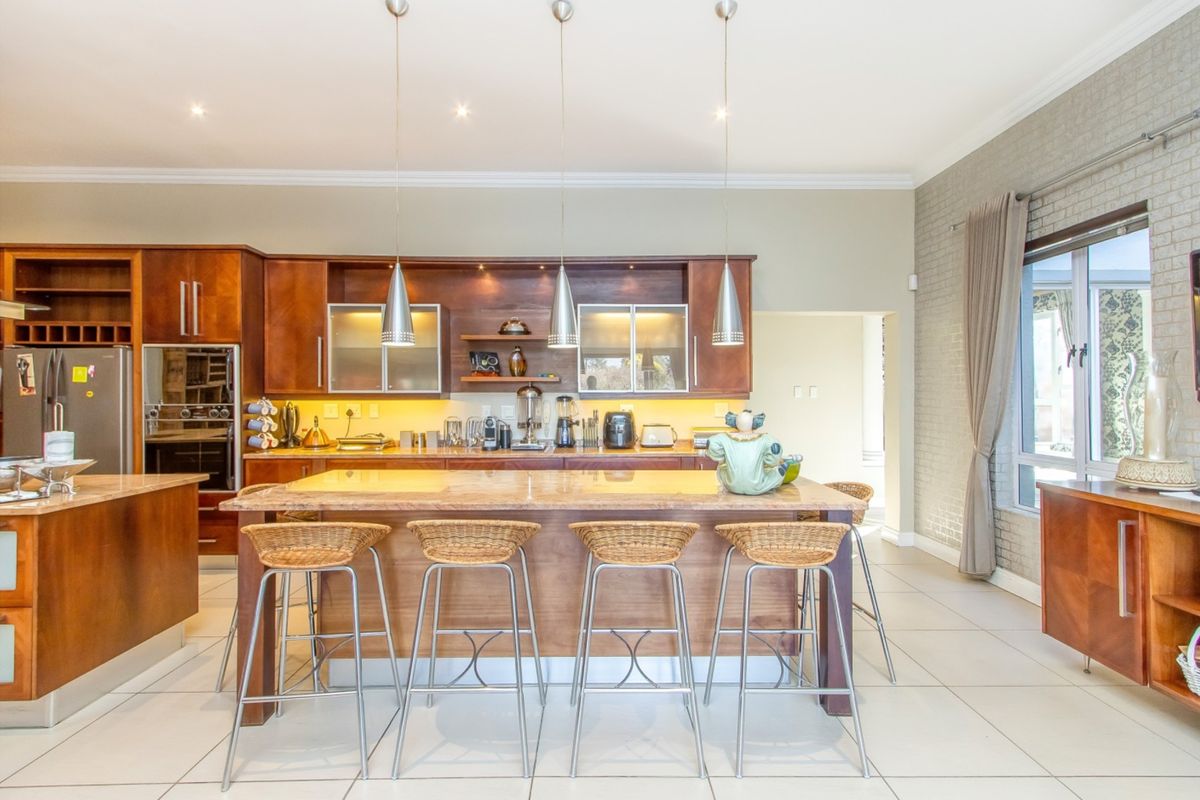 Spacious kitchen featuring warm wood cabinetry, stone countertops, a large central island with breakfast bar seating, and modern pendant lighting.