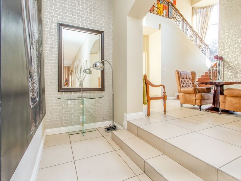Spacious entrance hall featuring tiled flooring, a textured feature wall, and an elegant staircase with decorative wrought iron railing.