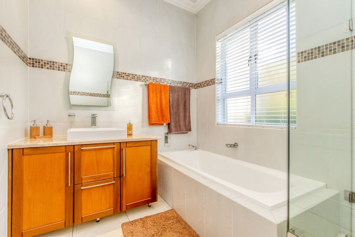 A well-maintained bathroom featuring a wooden vanity with a vessel sink, a built-in bathtub, and a glass-enclosed shower area with neutral wall tiling.