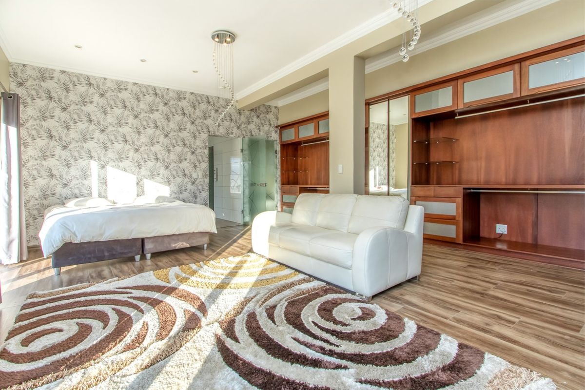 Spacious bedroom featuring extensive built-in wooden cabinetry, laminate flooring, crown molding, and an integrated glass-enclosed en-suite bathroom.