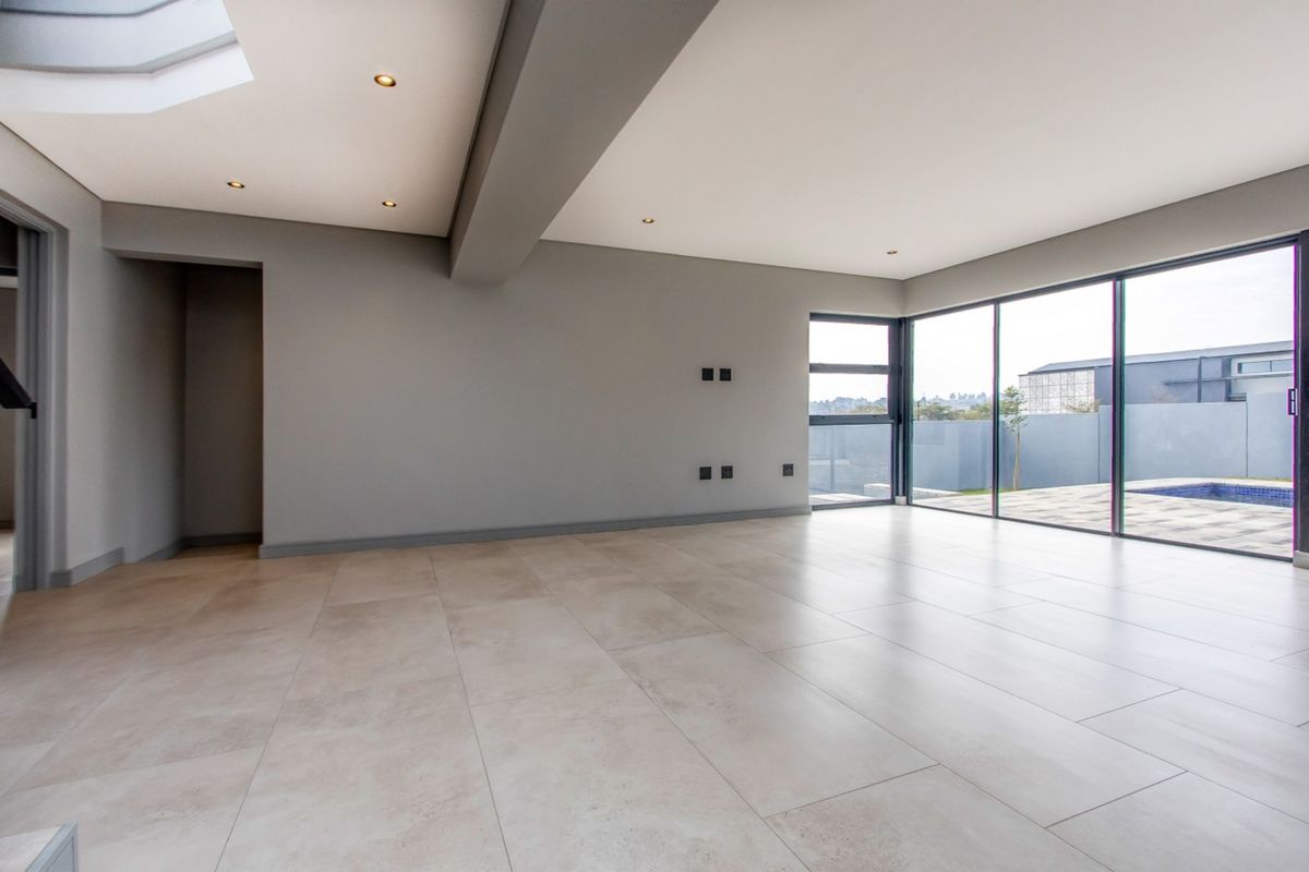 Spacious, modern open-plan living area featuring large format floor tiles, recessed lighting, a skylight, and expansive sliding doors leading to the outdoor pool area.