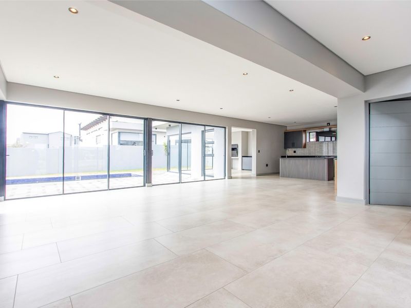 Spacious open-plan living area featuring large format floor tiles, recessed lighting, and expansive sliding glass doors that open to the pool area.