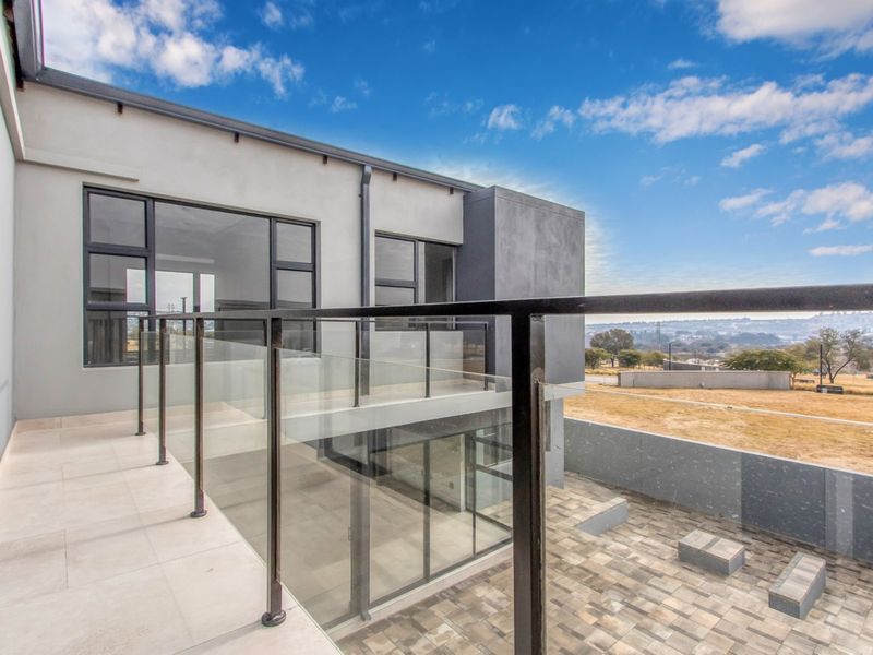 Modern elevated balcony featuring a sleek glass balustrade, tiled flooring, and large aluminium sliding doors overlooking a paved rear courtyard.