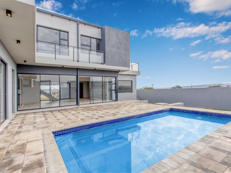 Modern double-story residence featuring a paved patio area, a swimming pool with blue mosaic tiling, and extensive glass sliding doors for indoor-outdoor flow.