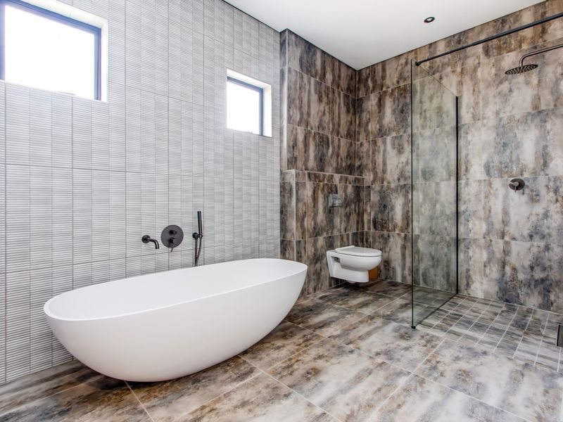 Modern bathroom featuring a sleek freestanding bathtub, a spacious walk-in shower with glass screen, and contemporary wall-mounted toilet with high-end tiled finishes.