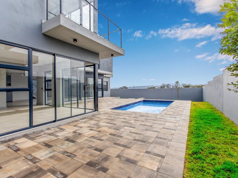 Modern rear exterior featuring a paved patio, swimming pool, and large sliding glass doors leading into the home.