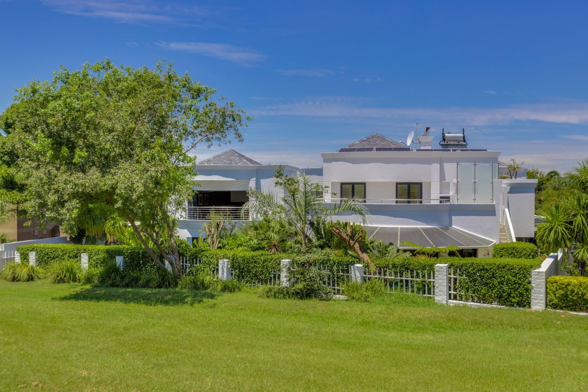 Rear view of a modern two-story house featuring a landscaped garden, metal fencing, a balcony with glass balustrades, and roof-mounted solar energy systems.