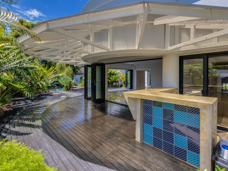 A spacious outdoor patio featuring timber decking, a built-in tiled bar, and seamless access to the interior through large bi-fold doors.
