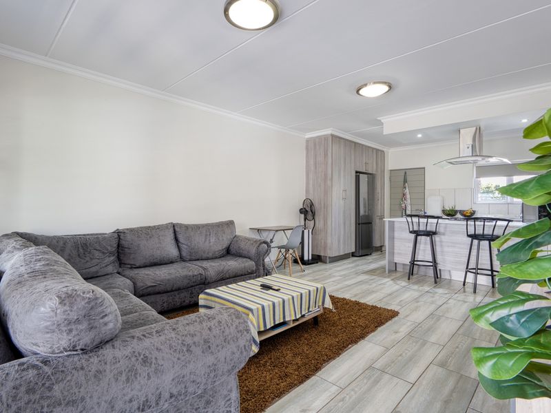 An open-plan living and kitchen area featuring modern wood-look cabinetry, a central kitchen island with breakfast bar, and neutral tiled flooring throughout.