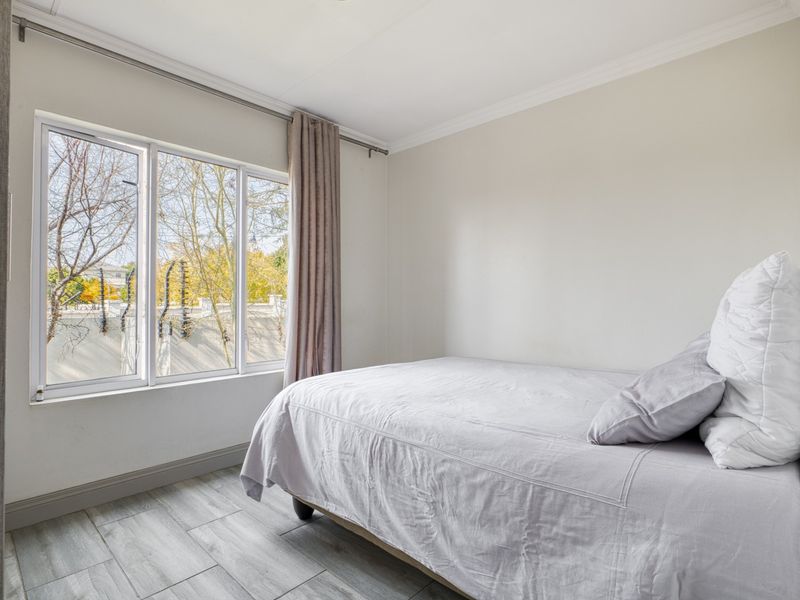 A bright and well-maintained bedroom featuring wood-look tile flooring, crown molding, and a large window providing natural light.
